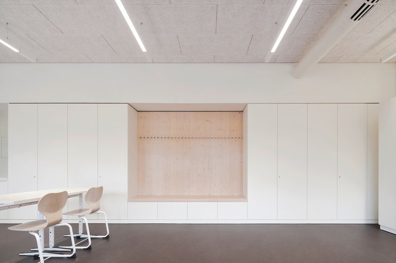 Built-in storage wall with recessed plywood niche and linear LED fixtures in the concrete ceiling