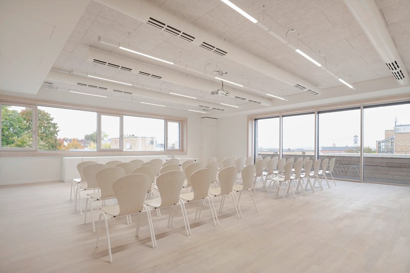 Conference space with rows of chairs facing floor-to-ceiling windows overlooking adjacent rooftops