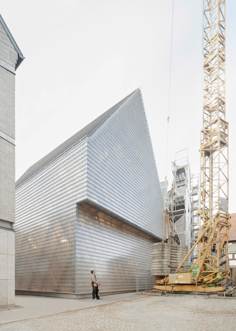 Street view showing the gabled glass brick facade beside a yellow construction crane