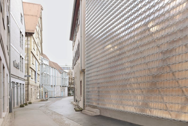 Narrow cobbled street with the textured glass brick wall rising alongside residential buildings