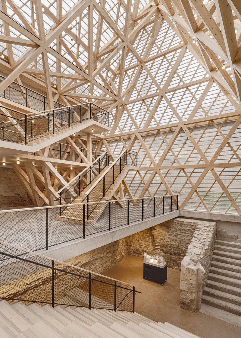 Multi-level interior showing crisscrossing staircases and exposed stone foundation walls beneath the timber lattice