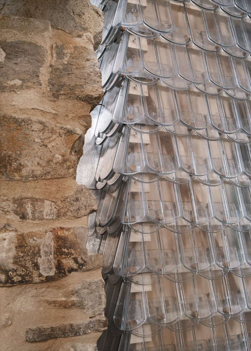 Detail of the translucent glass shingle facade meeting the excavated stone foundation wall