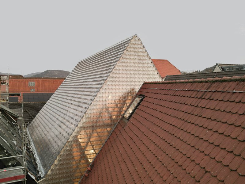 Pyramidal glass tile roof rising above surrounding red clay tile rooftops on an overcast day