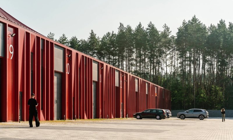 Vertical red metal fins along the warehouse facade with two parked cars and a person walking