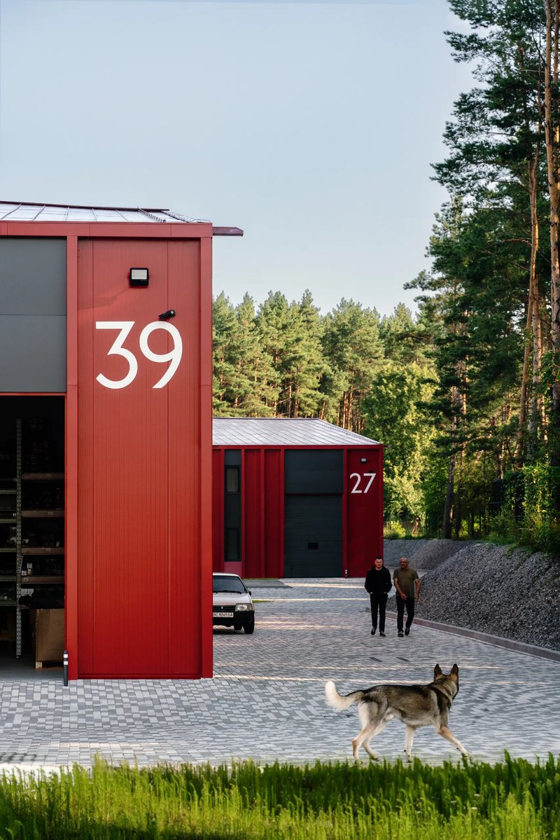 View of numbered red metal-clad units with a dog and people in a forested courtyard