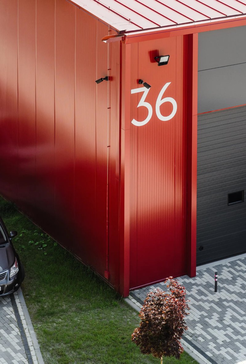 Red corrugated metal facade with white painted number 36 and a small shrub at the base