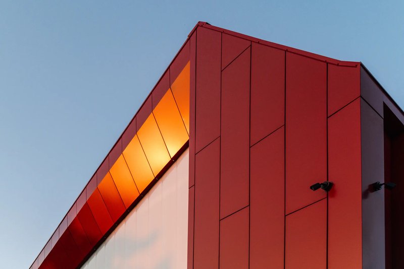 Upward view of the angled red metal panel soffit meeting the white wall at dusk