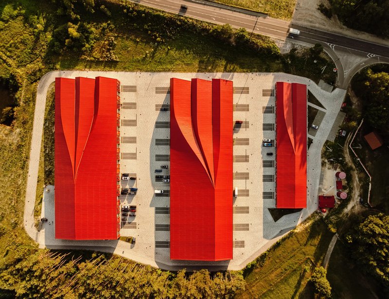 Drone view of three red corrugated roofs separated by parking bays and surrounded by forest
