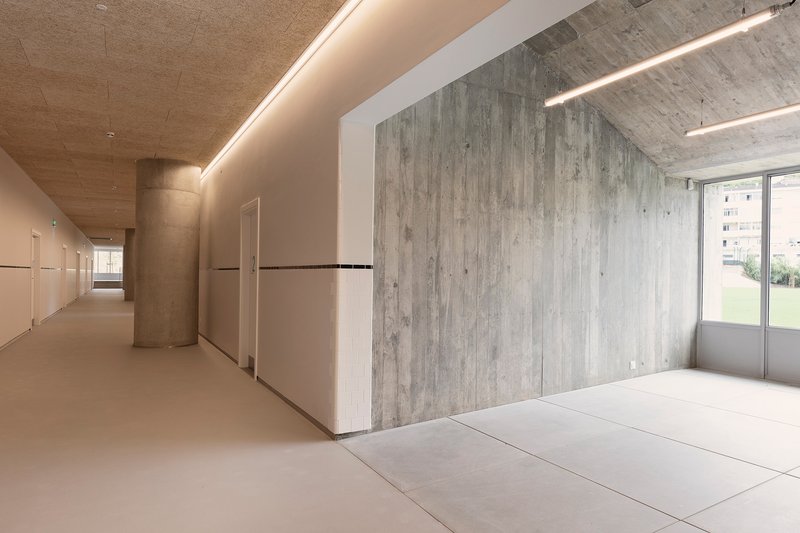 Corridor with board-formed concrete service core and continuous cove lighting along the ceiling edge