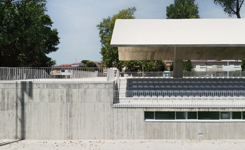 Board-marked concrete retaining walls and stadium seating tiers beneath the overhanging canopy structure