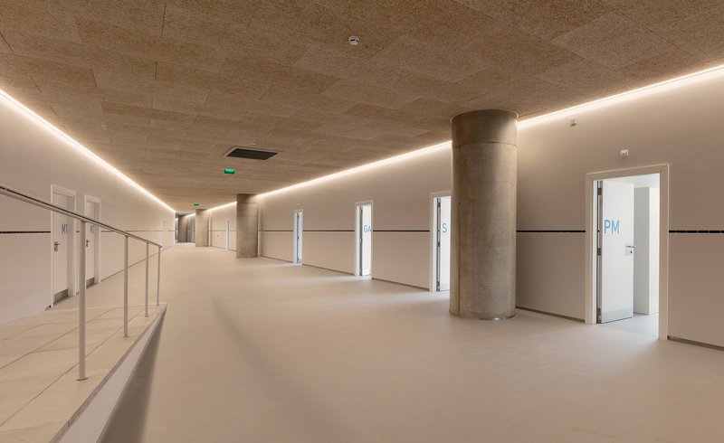 Interior concourse with continuous perimeter lighting along the board-marked concrete ceiling and circular columns