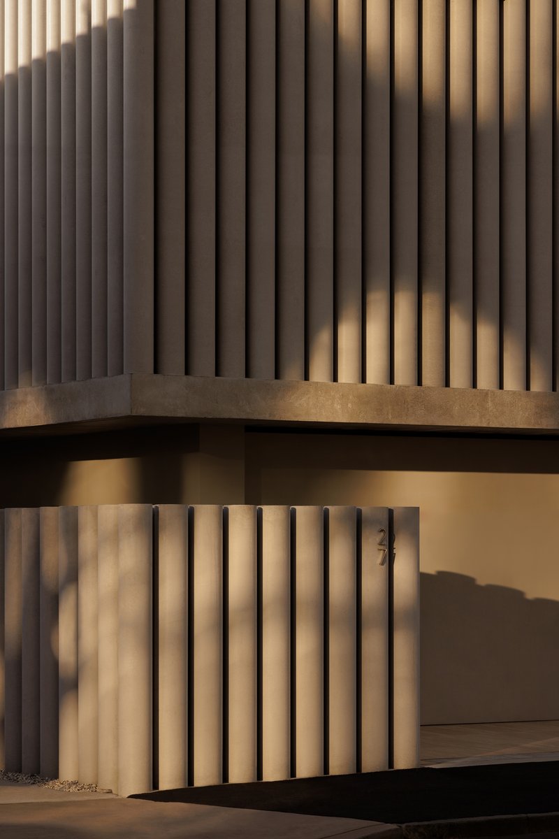 Facade detail showing vertical concrete fins with evening shadows cast across lower screen wall