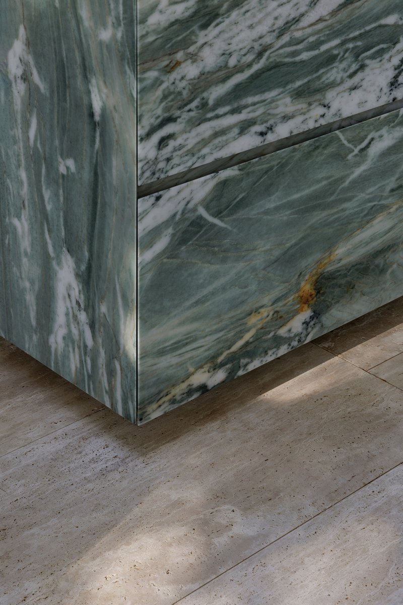 Corner detail of veined green marble panels meeting a travertine floor