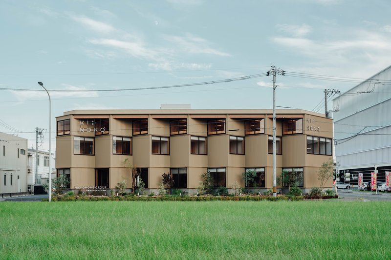 Street view of the corrugated metal facade with cylindrical bay windows across a rice field