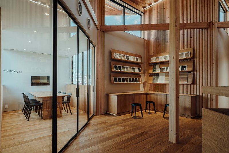 Reception area with timber post and beam structure and wall-mounted material samples beside glazed meeting room