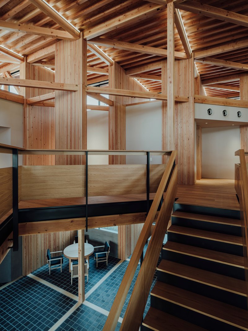 Double-height interior with exposed timber frame structure and mezzanine overlooking a blue-tiled lower level with seating