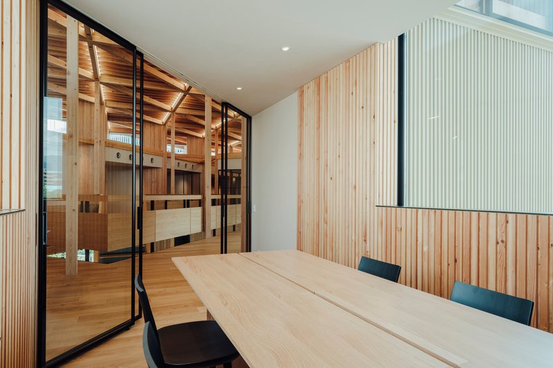 Conference room enclosed by vertical wood slats and black-framed glazing with view to sauna