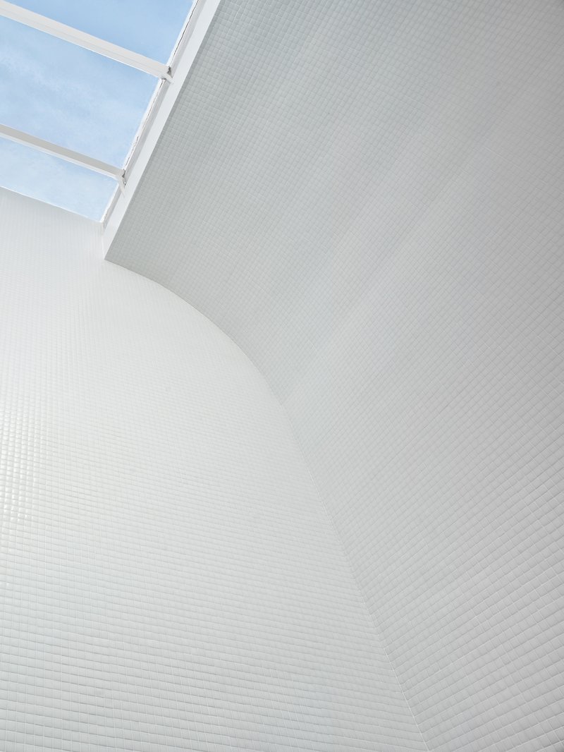 Curved white mosaic tile wall rising to a skylight under blue sky