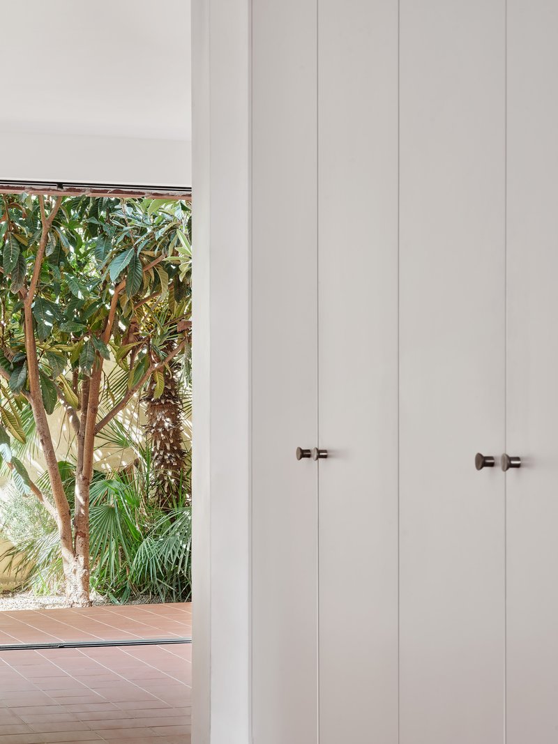 Floor-to-ceiling white storage cabinets with bronze knobs beside garden view window