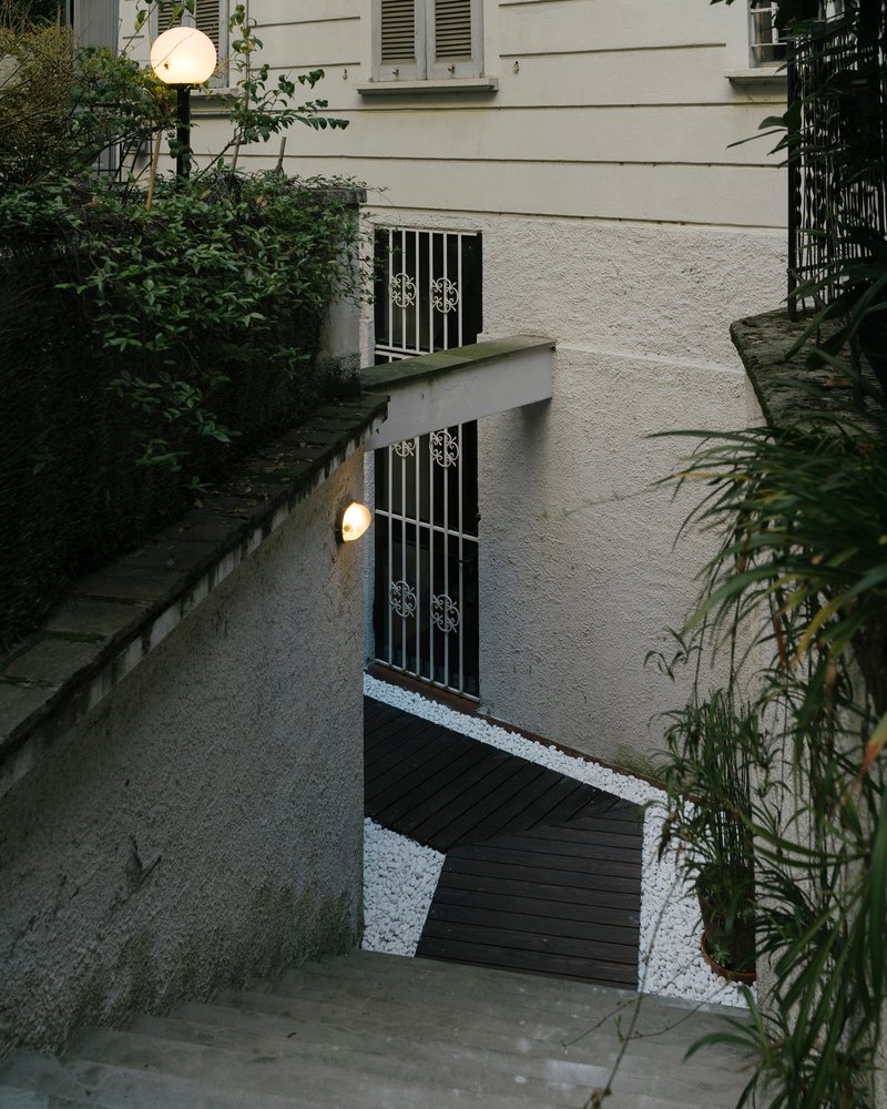 Top-down view of sunken courtyard with timber decking, white gravel, metal grilles, and wall-mounted spherical lights