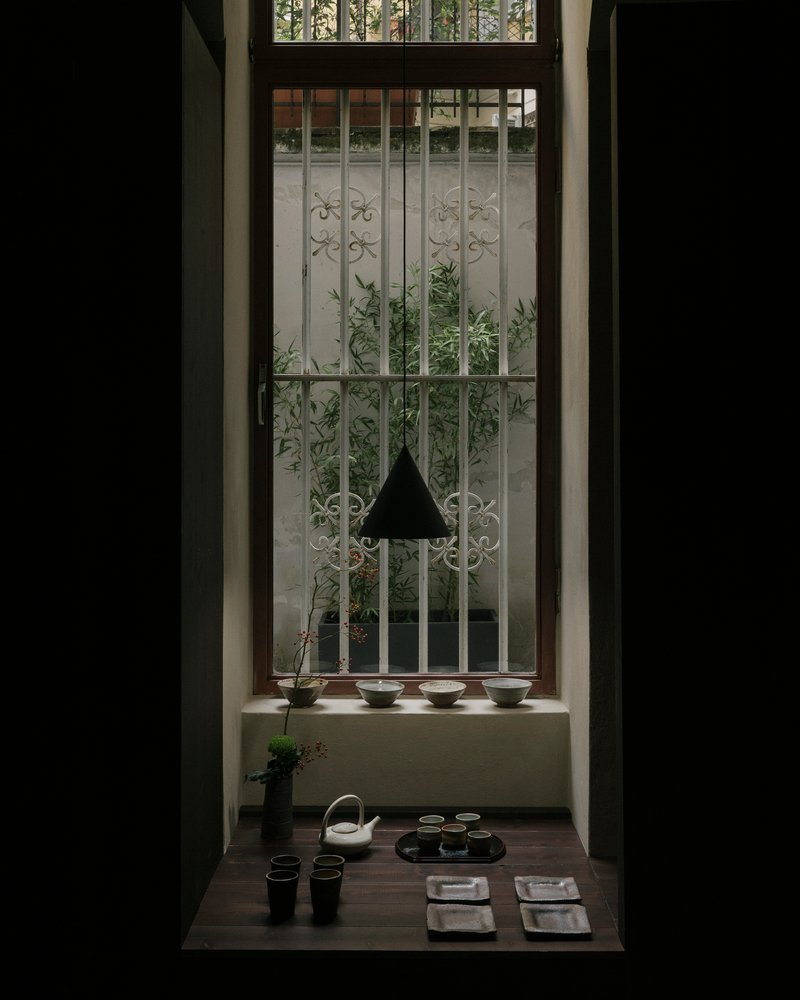Low table set for tea in front of window with decorative metal grille and planted courtyard beyond