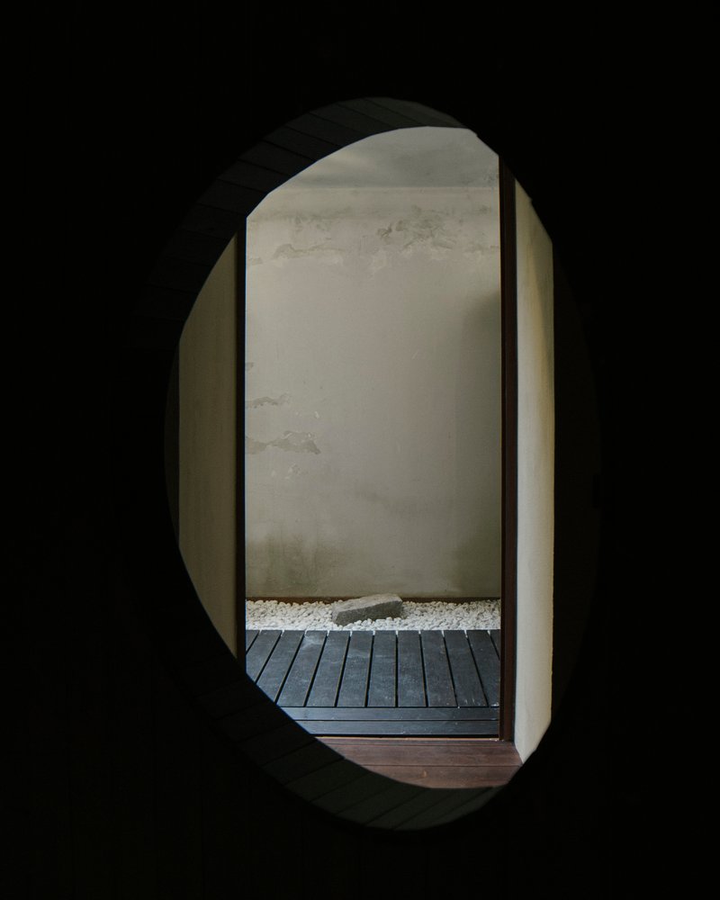 View through oval portal showing timber decking, white gravel bed, and rendered wall in daylight