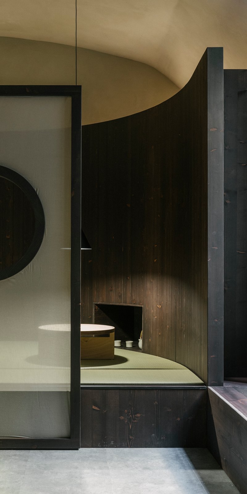 Glass partition framing a curved dark timber wall with built-in seating under vaulted ceiling
