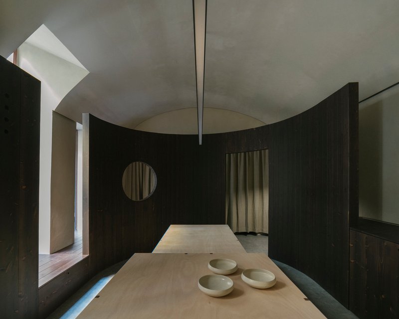 Interior room with dark timber partition, circular opening, and plywood table holding three ceramic bowls