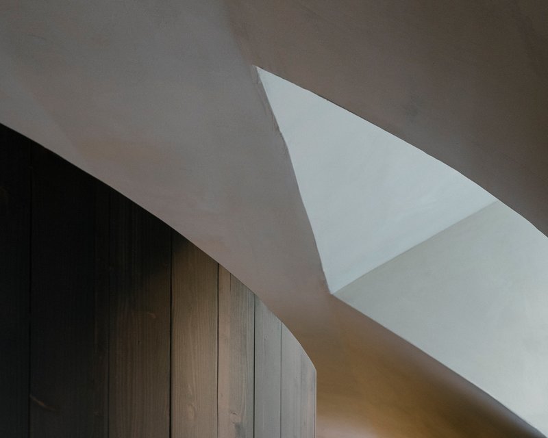 Triangular skylight piercing white plaster ceiling above dark timber wall paneling