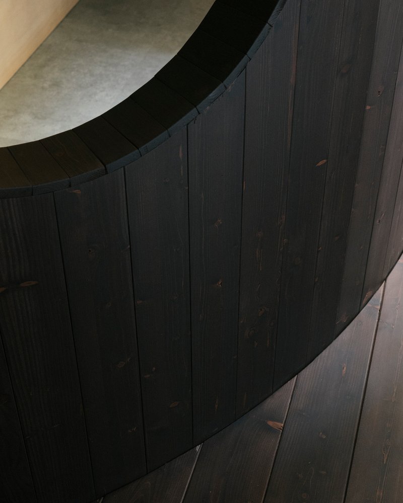 Close-up of curved charred timber wall with vertical planks meeting arched plaster ceiling