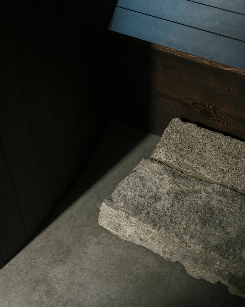 Grey concrete floor meeting a rough stone block and dark timber wall in soft daylight