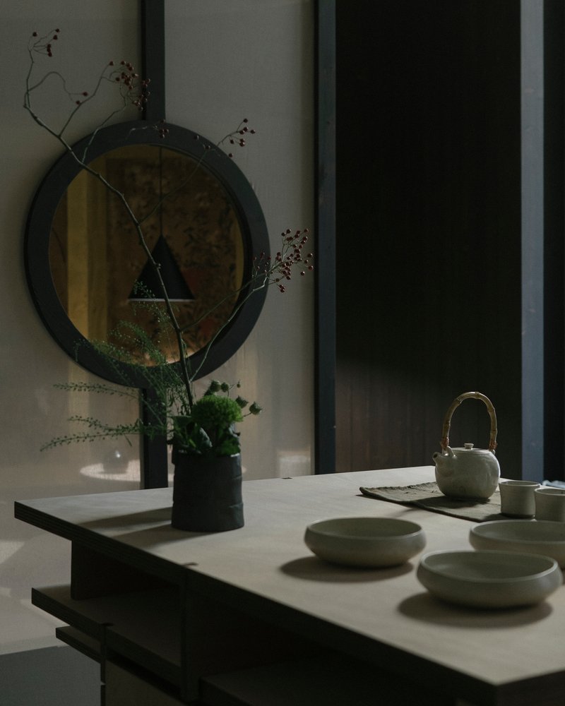 White countertop with ceramic tea set and dried branches reflected in a round mirror