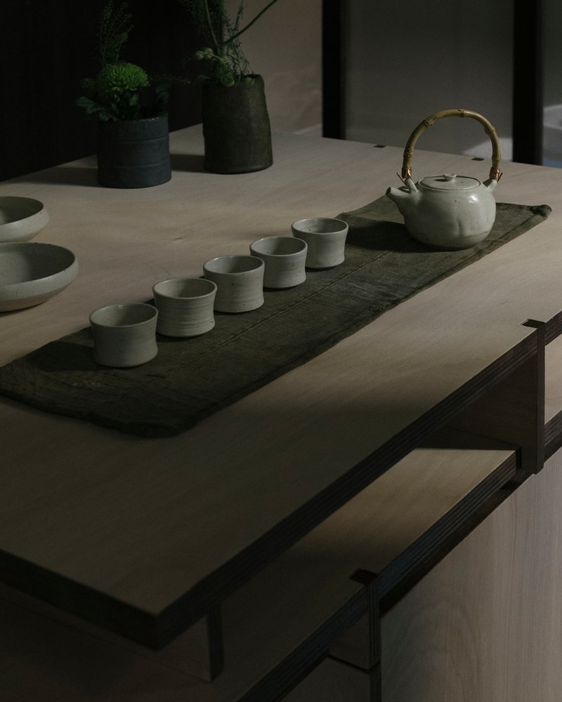 Tea ceremony arrangement with ceramic cups and teapot on a dark stone runner