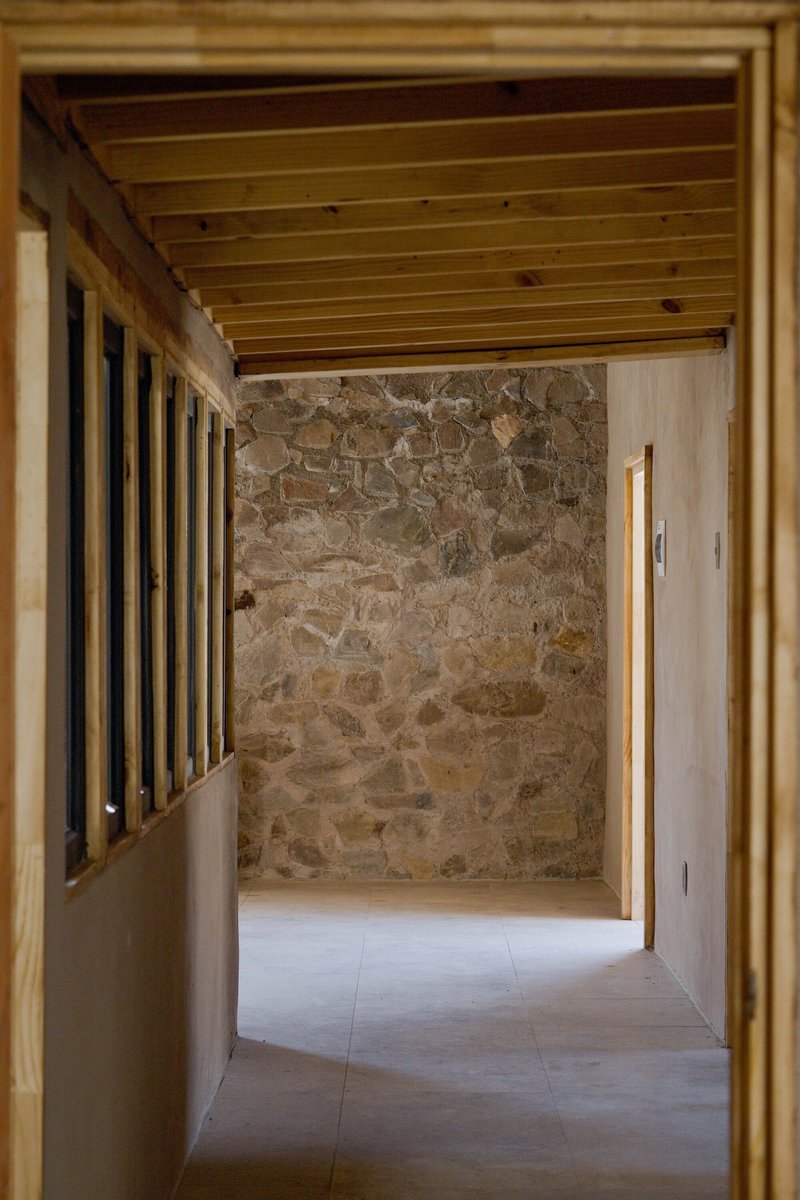Interior corridor with exposed timber ceiling beams, stone wall, and timber slat partition wall