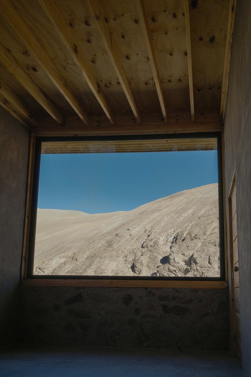 Square window framing the desert hillside beyond with exposed timber joists overhead