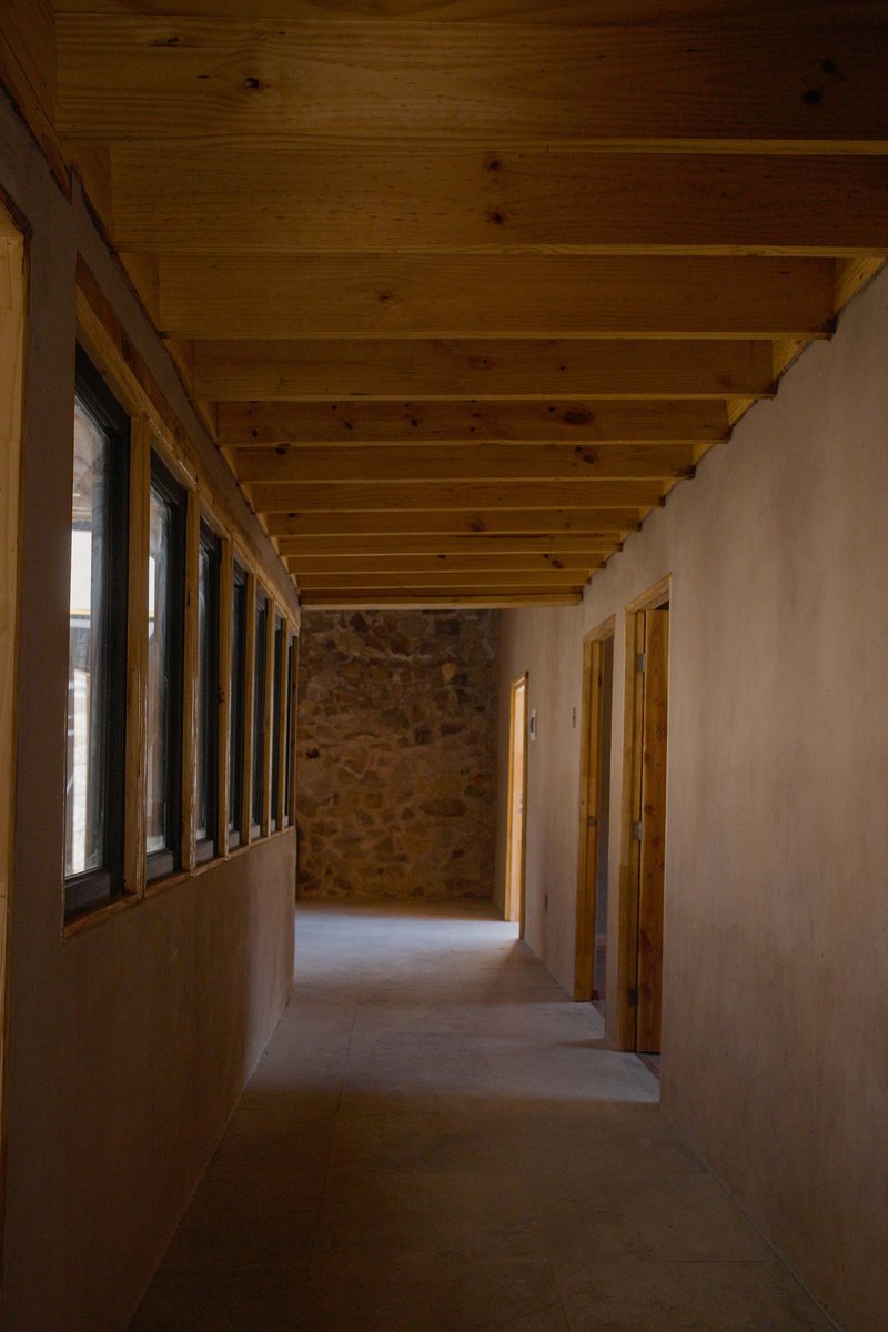 Interior corridor with exposed timber ceiling beams and stone accent wall lit by a ribbon of windows