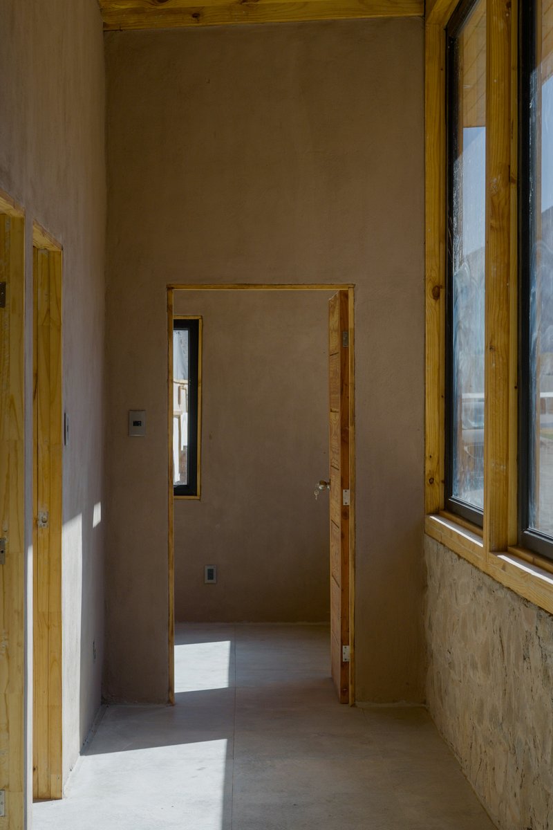 Hallway junction with timber-framed doorway and narrow vertical window casting sunlight across plastered walls