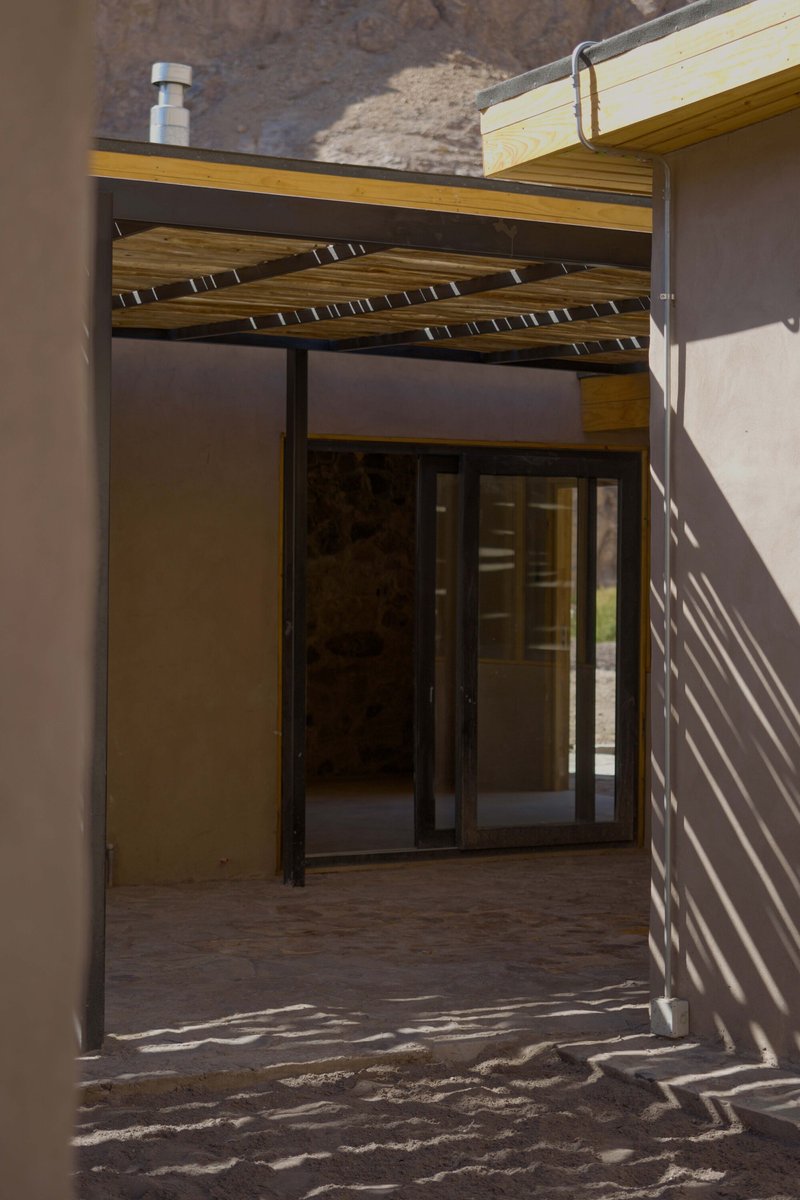 Exterior courtyard entry with timber slat pergola casting shadows over sliding glass doors and stone pavers