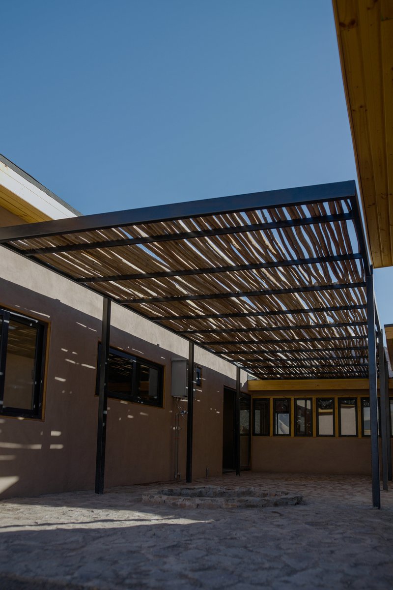 Sheltered courtyard with slatted steel overhead canopy filtering daylight onto plastered walls and stone paving