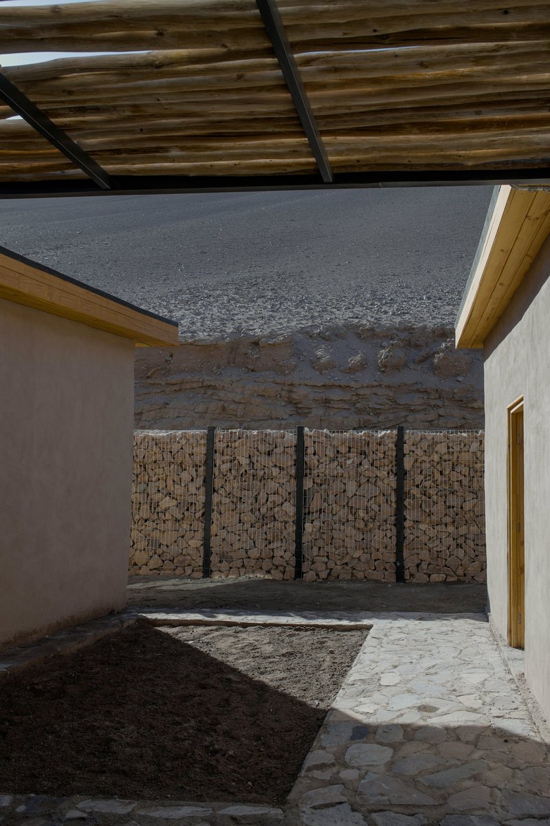 Interior courtyard with stone-filled gabion wall and earth mound under a timber pergola