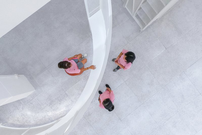 Aerial view of three visitors in pink shirts on a pale terrazzo floor beside a curved white balustrade