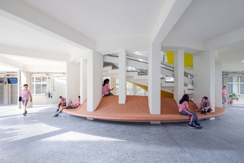 Students gathered on the terraced cork seating platform beneath white columns and exposed ductwork