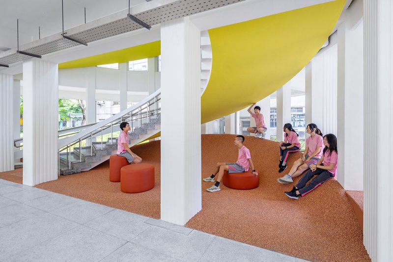 Cork terrazzo seating landscape with yellow ceiling panels and orange upholstered stools beside the staircase