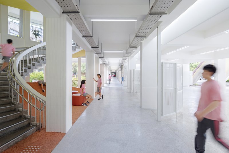 White corridor with exposed mechanical systems and students moving past the cork seating nook