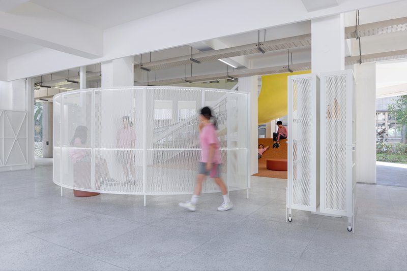 Curved perforated white metal screen enclosing the terrazzo seating area with students in motion