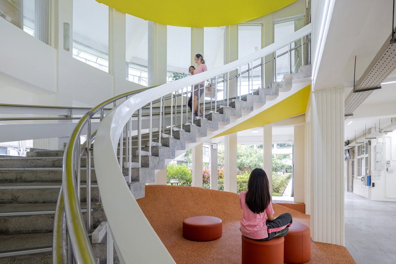 Helical staircase with yellow metal railings ascending beside the cork platform under a yellow ceiling disc