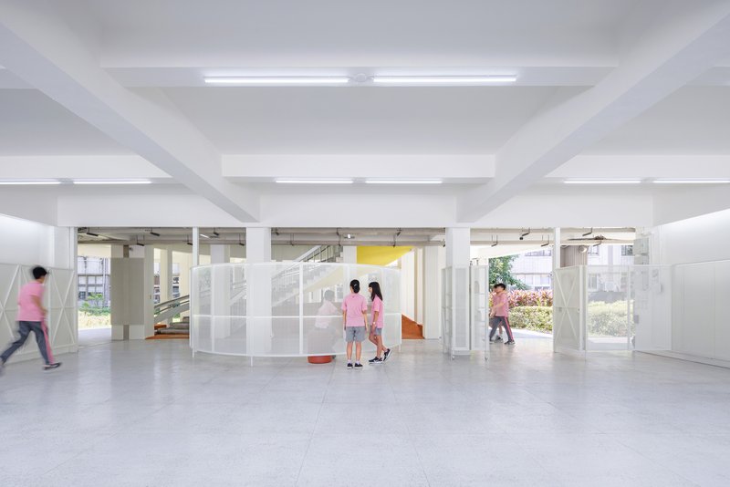 Open ground floor space with white columns and translucent partition panels as students pass through