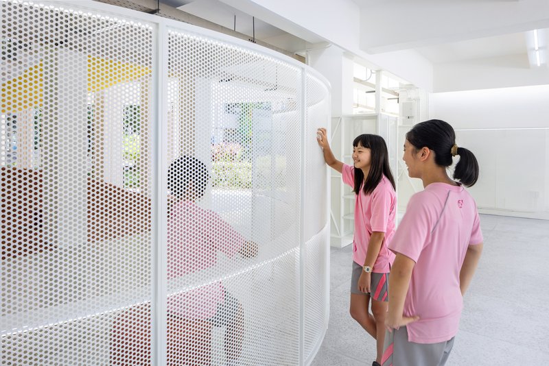 Two students examining a white perforated metal partition screen with colorful views beyond