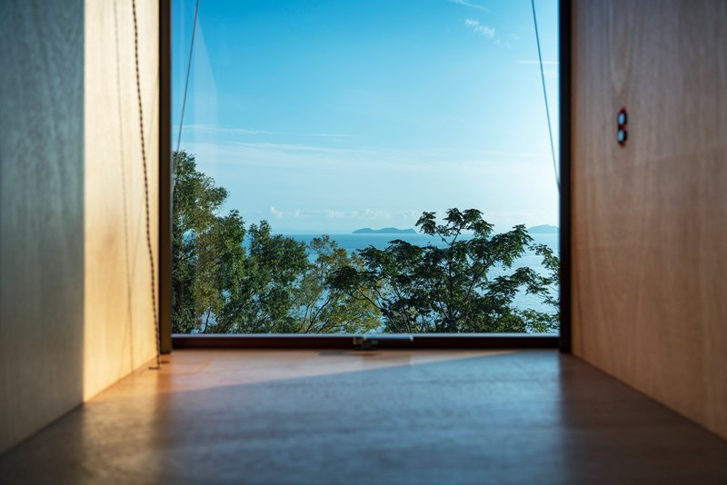 Floor-level view through a window framing treetops and ocean islands under clear sky