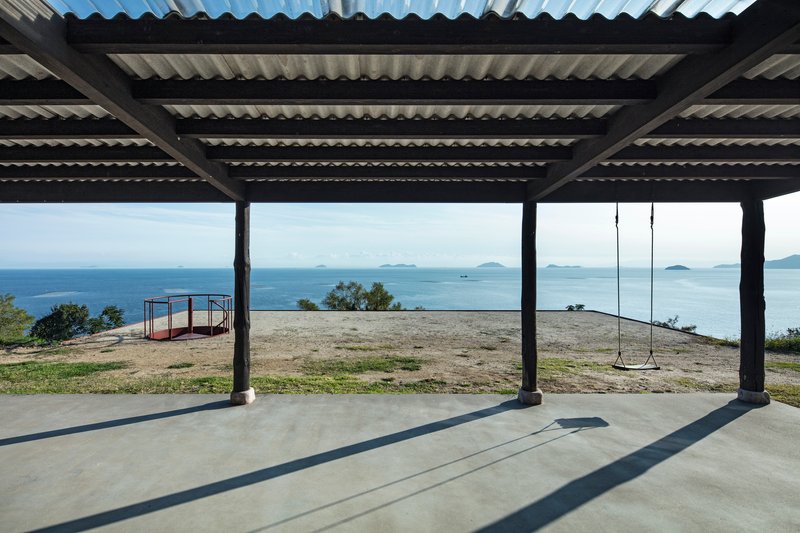 Covered terrace with corrugated roof and steel columns overlooking coastal landscape with swing